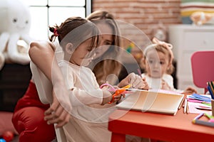 Teacher with girls sitting on table cutting paper at kindergarten