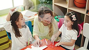 Teacher with girls sitting on table having handcrafts class at kindergarten