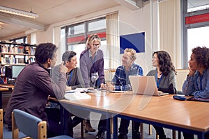 Teacher With Group Of Mature Adult Students In Class Sit Around Table And Work In College Library