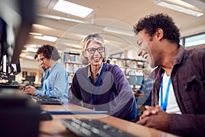 Teacher With Group Of Mature Adult Students In Class Working At Computers In College Library