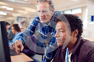 Teacher With Group Of Mature Adult Students In Class Working At Computers In College Library