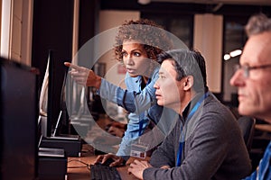 Teacher With Group Of Mature Adult Students In Class Working At Computers In College Library