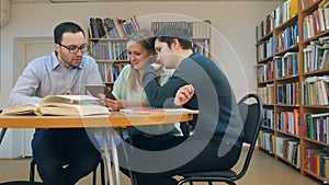 Teacher with group of students working on digital tablet in library