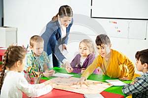 Teacher and happy children sitting at table with board game and dice in school