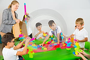 Teacher and happy schoolkids playing building blocks