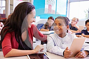 Teacher helping elementary school boy using tablet computer