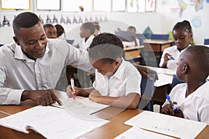 Teacher helping elementary school girl at her desk in class