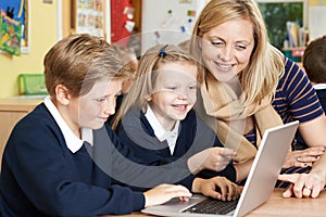 Teacher Helping Elementary School Pupils In Computer Class