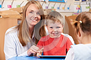 Teacher Helping Elementary Scool Pupil To Use Digital Tablet