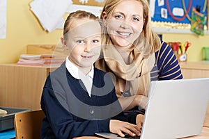 Teacher Helping Female Elementary School Pupil In Computer Class