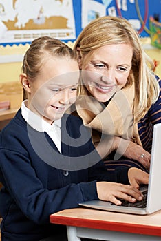 Teacher Helping Female Elementary School Pupil In Computer Class