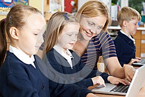 Teacher Helping Female Elementary School Pupils In Computer Class