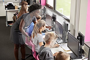 Teacher Helping Female Pupil Line Of High School Students Working at Screens In Computer Class