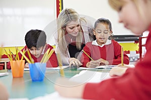 Teacher Helping Female Pupil With Writing Reading At Desk