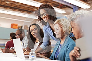 Teacher Helping Group Of Retired Senior Women Attending IT Class In Community Centre