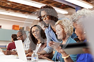 Teacher Helping Group Of Retired Senior Women Attending IT Class In Community Centre