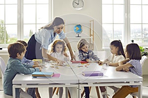 Teacher helping little primary school children group join puzzle in classroom