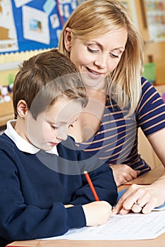 Teacher Helping Male Elementary Pupil Working At Desk