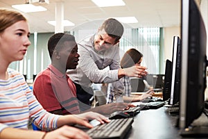 Teacher Helping Male High School Student Working In Computer Class