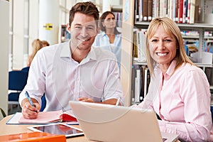 Teacher Helping Mature Student With Studies In Library