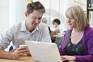 Teacher Helping Mature Student With Studies In Library