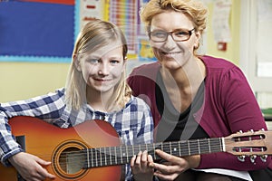 Teacher Helping Pupil To Play Guitar In Music Lesson