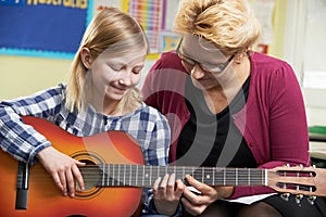 Teacher Helping Pupil To Play Guitar In Music Lesson