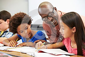 Teacher Helping Pupils Studying At Desks In Classroom