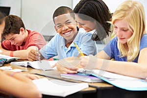 Teacher Helping Pupils Studying At Desks In Classroom