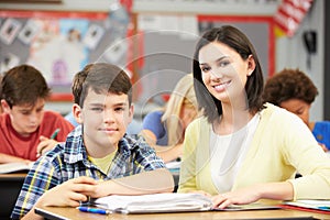 Teacher Helping Pupils Studying At Desks In Classroom