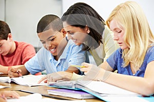 Teacher Helping Pupils Studying At Desks In Classroom