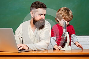 Teacher helping pupils studying on desks in classroom. Young boy doing his school homework with his father. Chalkboard