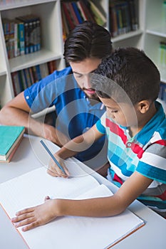 Teacher helping school kid with his homework in library