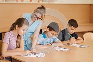 Teacher helping school kids writing test in classroom. education, elementary school, learning and people concept