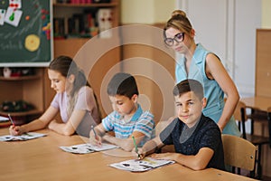 Teacher helping school kids writing test in classroom. education, elementary school, learning and people concept