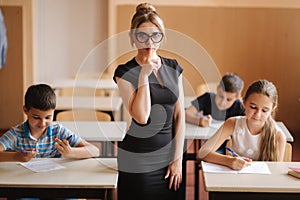 Teacher helping school kids writing test in classroom. education, elementary school, learning and people concept