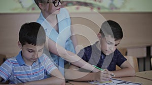 Teacher helping school kids writing test in classroom. education, elementary school, learning and people concept