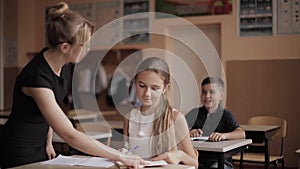 Teacher helping school kids writing test in classroom. education, elementary school, learning and people concept