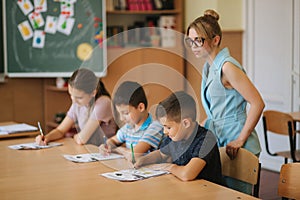 Teacher helping school kids writing test in classroom. education, elementary school, learning and people concept. Two