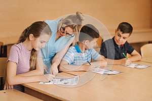 Teacher helping school kids writing test in classroom. education, elementary school, learning and people concept. Two