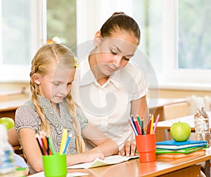 Teacher helping schoolgirl with schoolwork in classroom photo