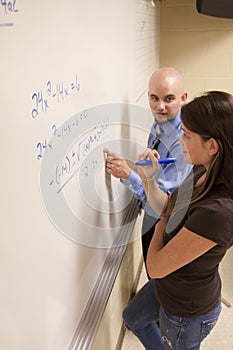 Teacher helping student with a math problem on a whiteboard.