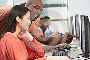 Teacher Helping Students Working At Computers In Classroom