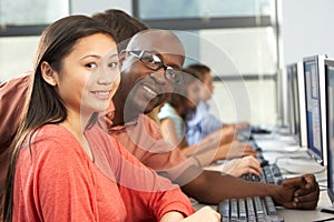 Teacher Helping Students Working At Computers In Classroom