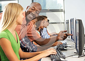 Teacher Helping Students Working At Computers In Classroom