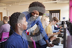 Teacher Helping Teenage Male High School Student Working In Computer Class