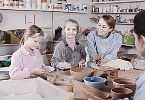 teacher helping teenagers at making pottery during arts and crafts class