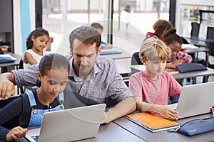 Teacher helping young students using laptops in class