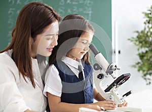 Teacher helps child to conduct experiment with microscope