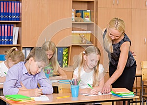 Teacher helps the schoolkids with schoolwork in classroom